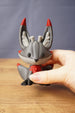 Obsidian Kitsuu collectible held in hand showing grey face, red chest detail, white inner ears and dark paws close up