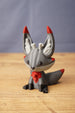 Obsidian Kitsuu fox figure seated front view with grey body, red ear tips, red chest detail and fantasy creature styling