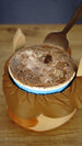 Close-up of a packaged ice cream tub placed inside the Ormuu character holder, showing the brown fringe around the rim and space for a spoon.