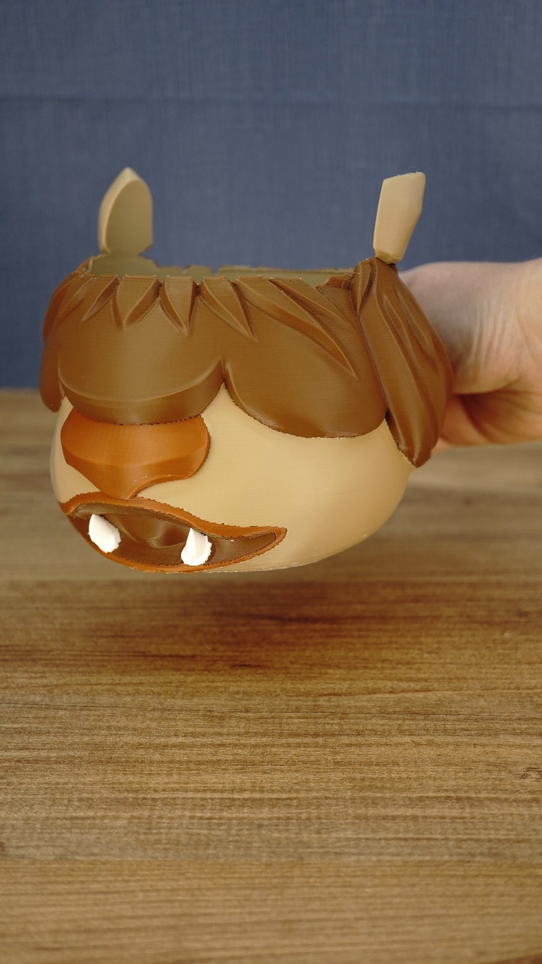 Ormuu Shack ice cream tub holder being lifted to demonstrate its size, rounded character body, detailed fringe and integrated side handle.