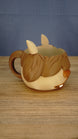 Side view of the Ormuu Shack character ice cream tub holder showing its large brown handle, layered fringe, cream body and small muzzle.