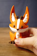 Hand holding an orange and white Ancient Kitsuu-inspired 3D-printed fox figure to demonstrate its size.