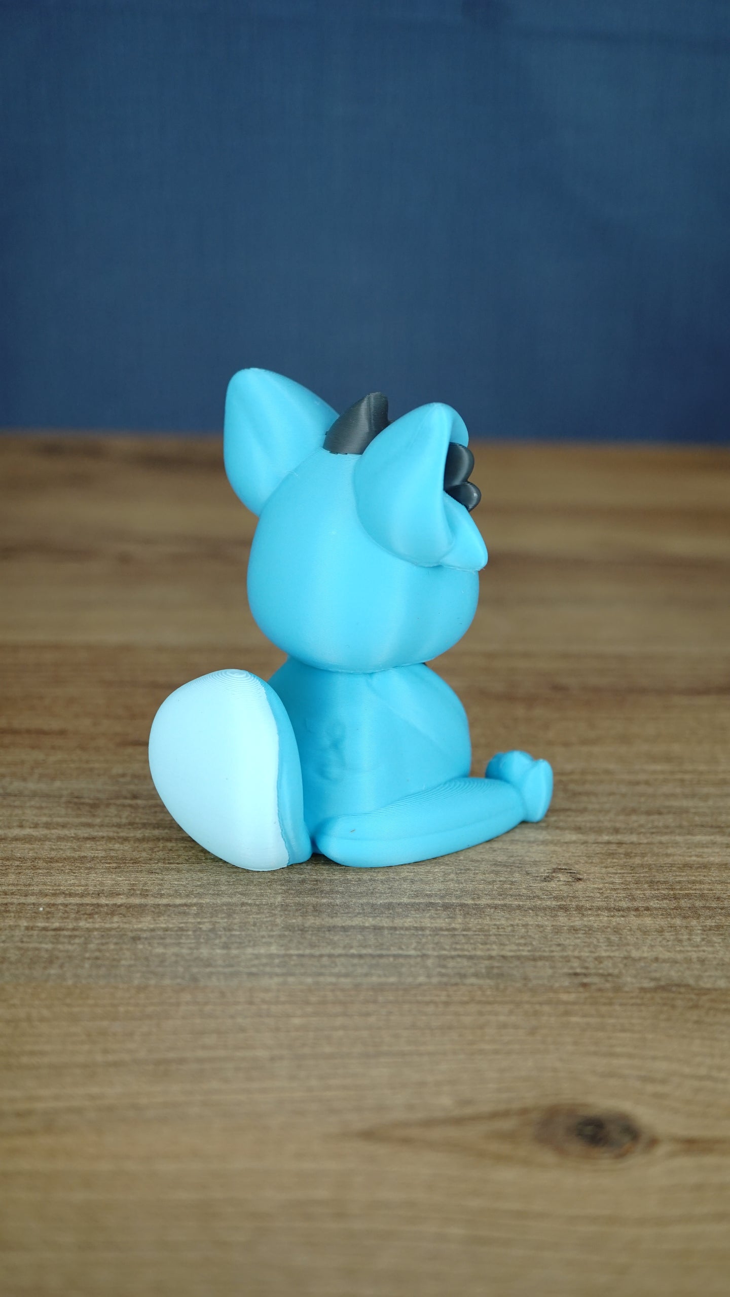 Back side view of a blue 3D printed Palcat plush figure showing its curled white-tipped tail, large ears, and seated pose.