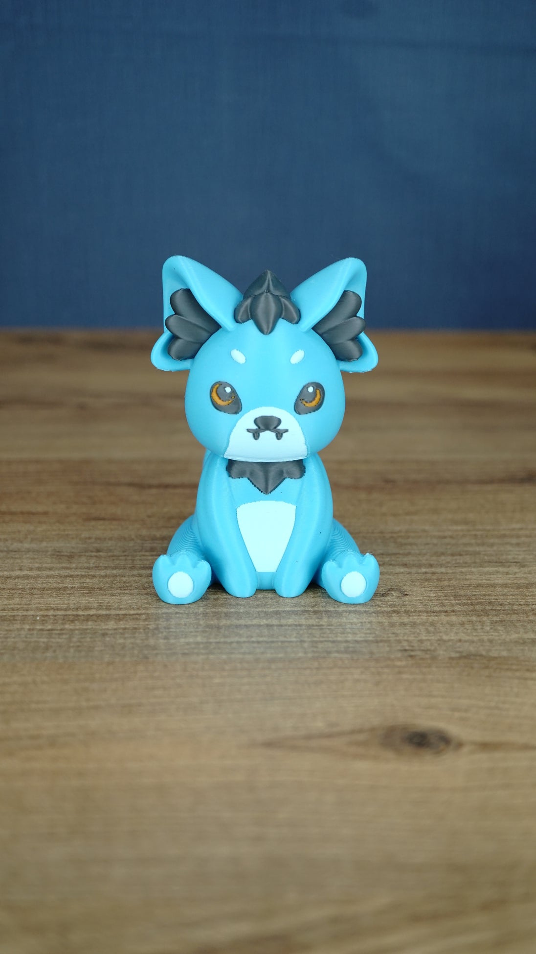 Front view of a blue 3D printed Palcat plush figure with amber eyes, dark grey accents, white muzzle, tiny fangs, and white paw pads.