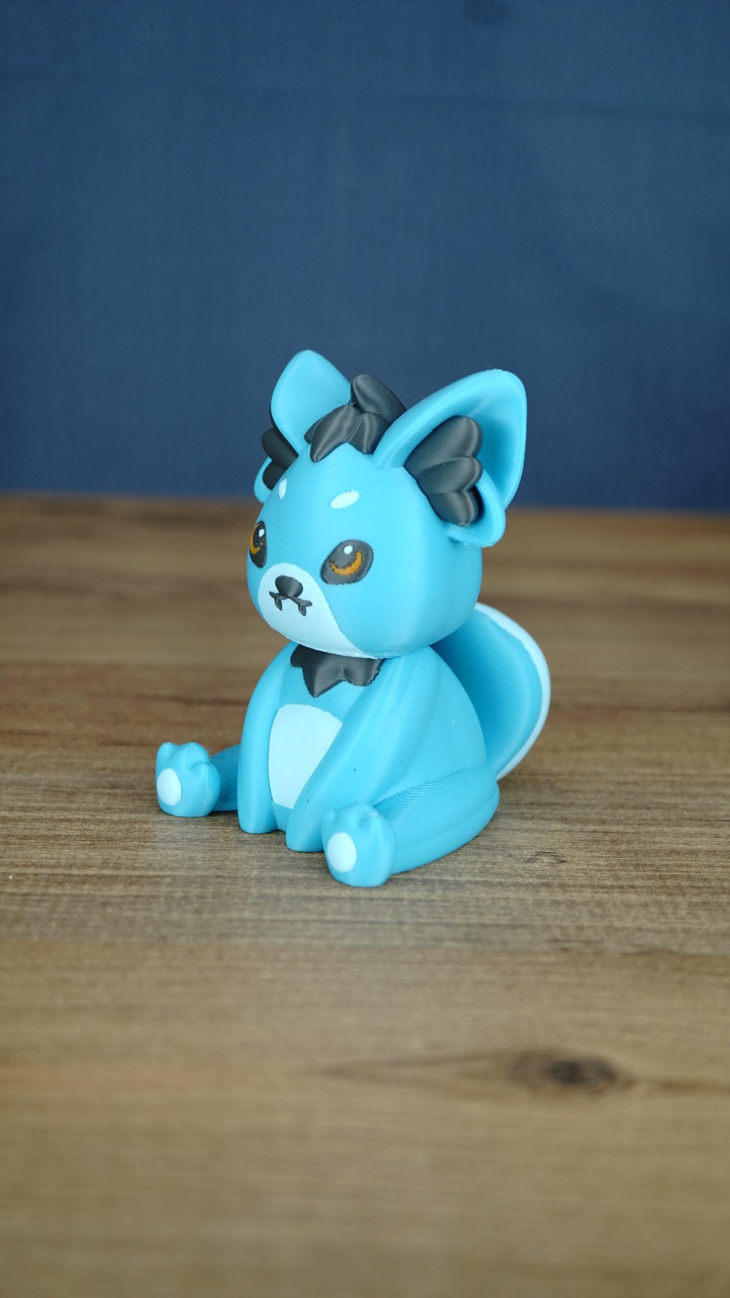 Side view of a blue 3D printed Palcat plush figure showing dark grey ear tufts, amber eyes, white chest detail, and curled tail.