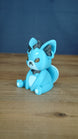 Side view of a blue 3D printed Palcat plush figure showing dark grey ear tufts, amber eyes, white chest detail, and curled tail.