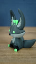 Profile view of a Cave Kitsuu 3D printed figure with tall ears, green eyes, black paws, and a curled tail.