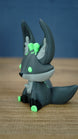 Profile view of a Cave Kitsuu 3D printed figure with tall ears, green eyes, black paws, and a curled tail.