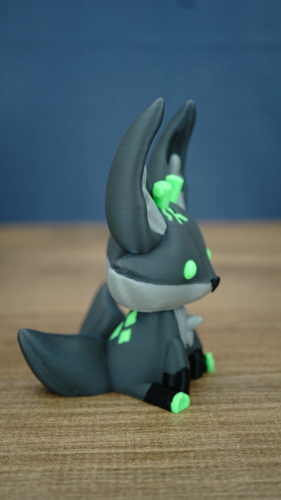 Side view of a Cave Kitsuu 3D printed figure showing its tall ears, dark green body, curled tail, and bright green accents.
