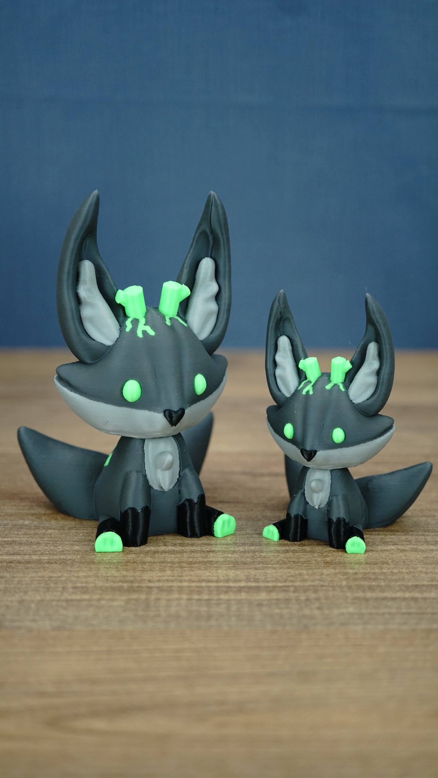 Large and small Cave Kitsuu 3D printed figures side by side, featuring dark green bodies, bright green accents, tall ears, and curled tails.