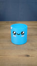 Front view of the blue Palia Cyl Cylinder Collectible with black eyes, a smiling face, and pink cheeks.