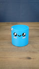 Front view of the blue Palia Cyl Cylinder Collectible with black eyes, a smiling face, and pink cheeks.