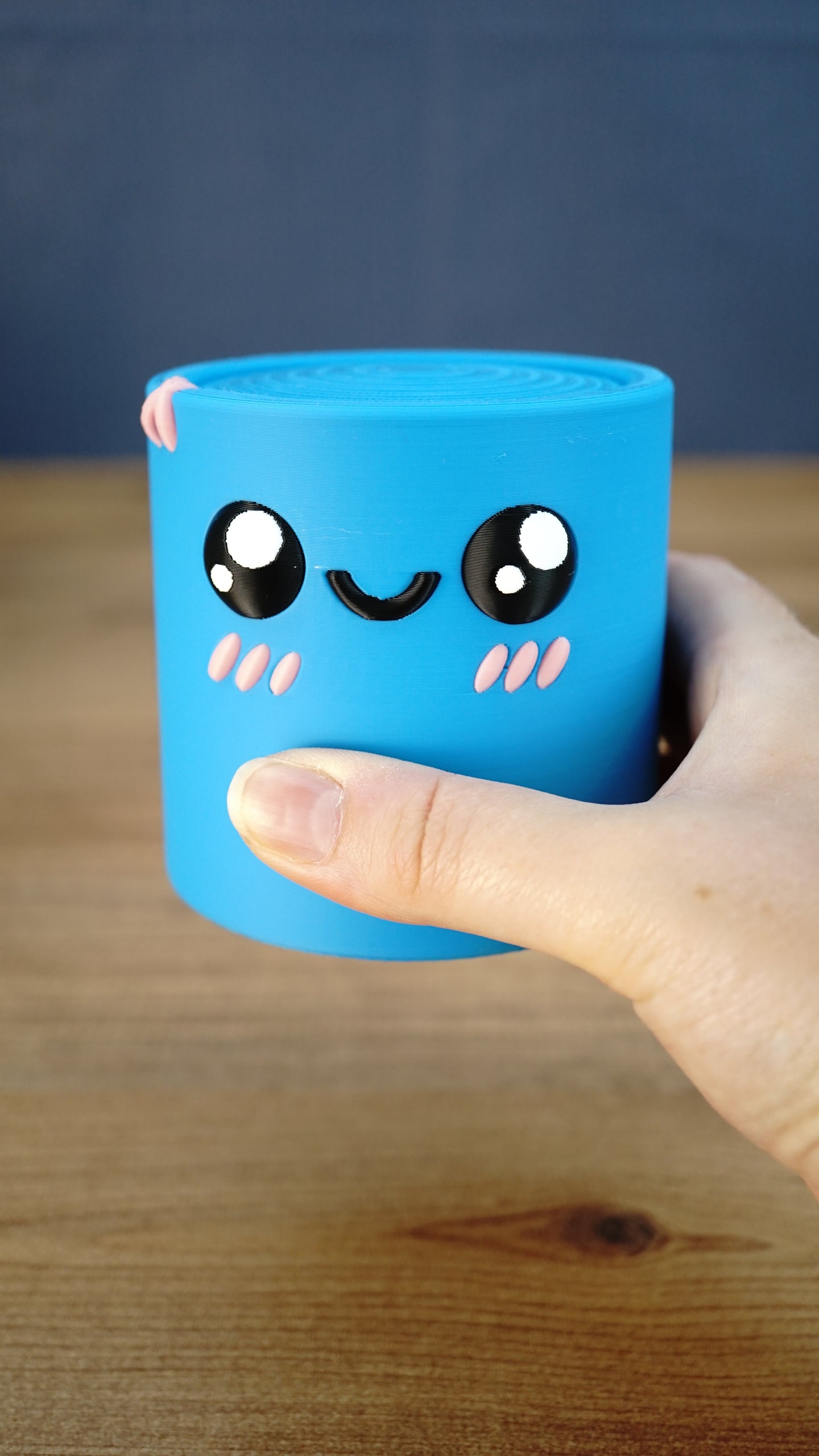 Close-up of the blue Palia Cyl Cylinder Collectible being held in a hand, showing its smooth 3D printed finish and kawaii face.