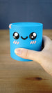 Close-up of the blue Palia Cyl Cylinder Collectible being held in a hand, showing its smooth 3D printed finish and kawaii face.
