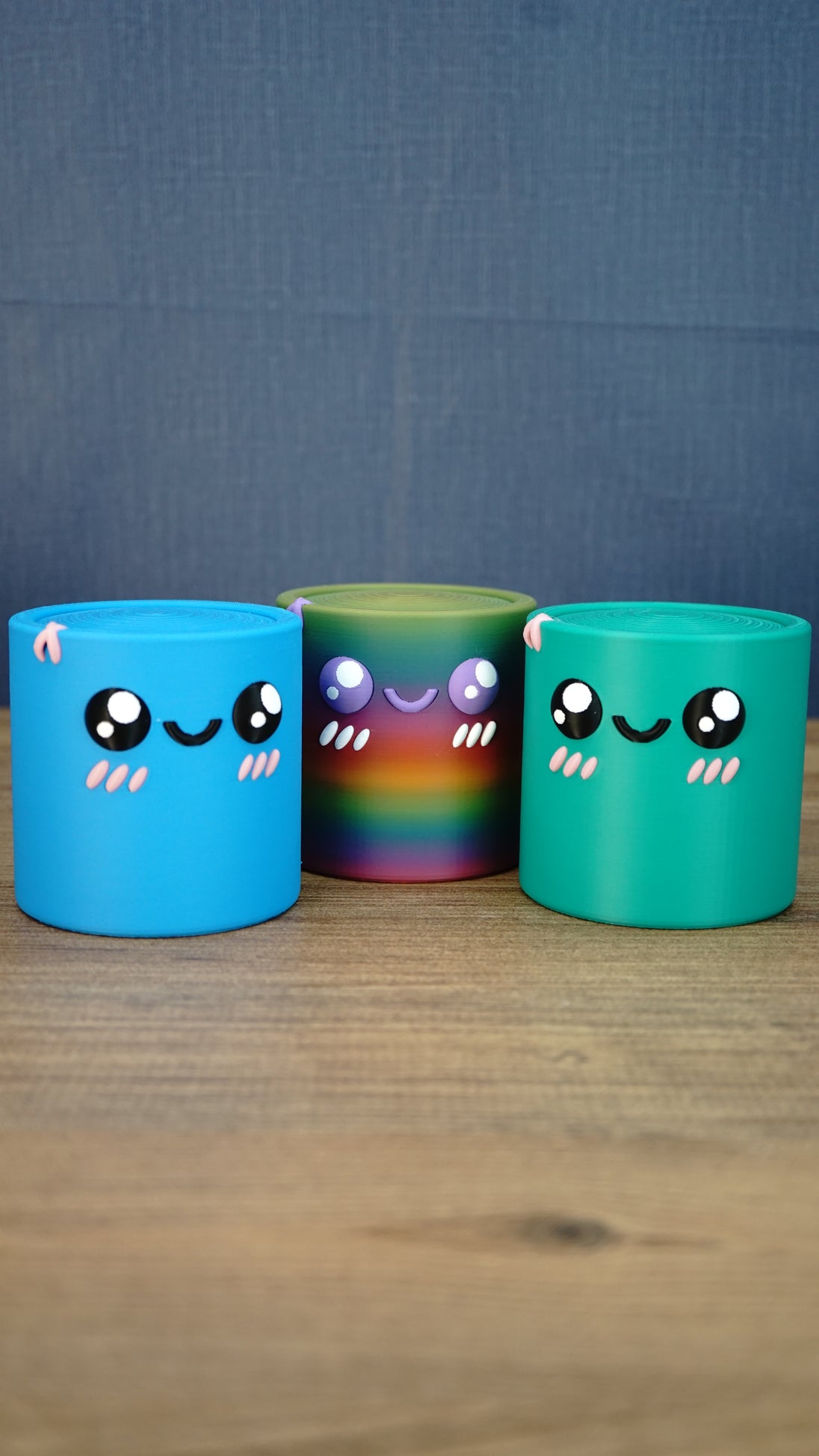 Blue Palia Cyl Cylinder Collectible displayed with the rainbow and green Cyl color versions on a wooden tabletop.