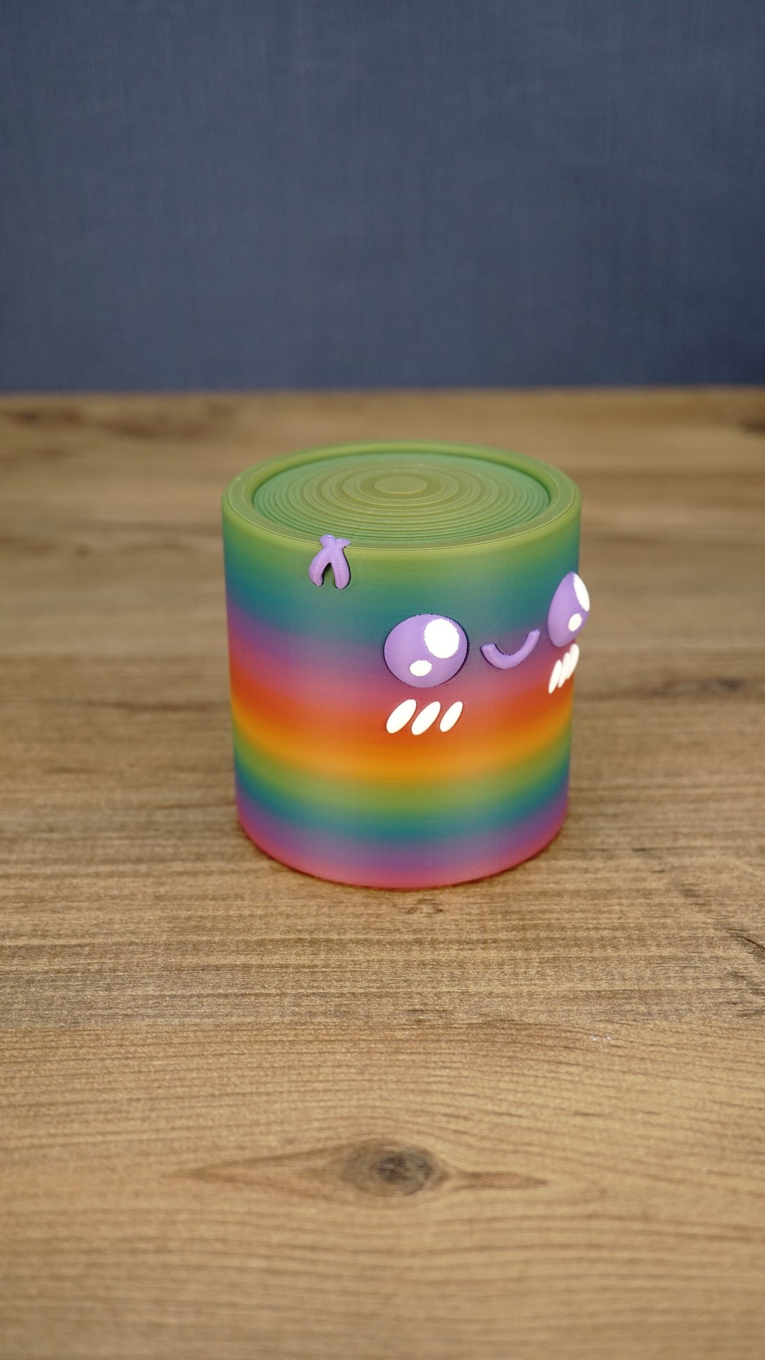 Angled view of a rainbow Palia Cyl Cylinder collectible showing the colorful striped body, spiral top texture, and cute face details.