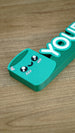 Close-up of cute green Cyl-inspired character beside raised personalized lettering on a custom Palia gamer nameplate for desks and shelves