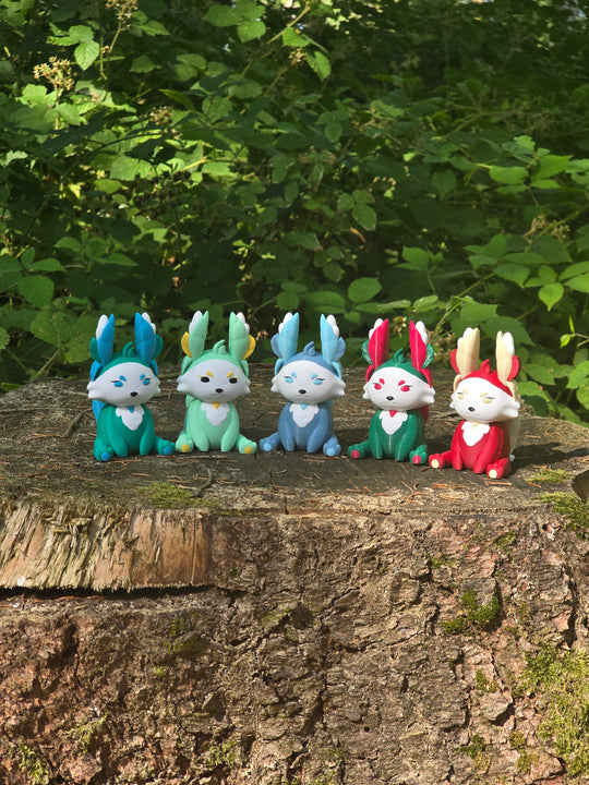 Five colourful 3D printed Palia Flutterfox plush figures displayed in a row on a tree stump in a forest.