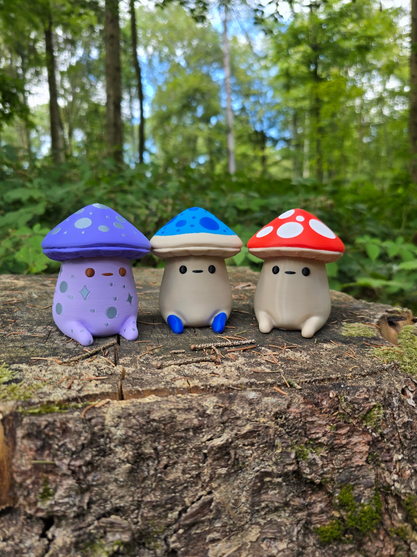 Three Palia Fun Guy 3D printed figurines with purple, blue, and red mushroom caps displayed on a tree stump in a forest.