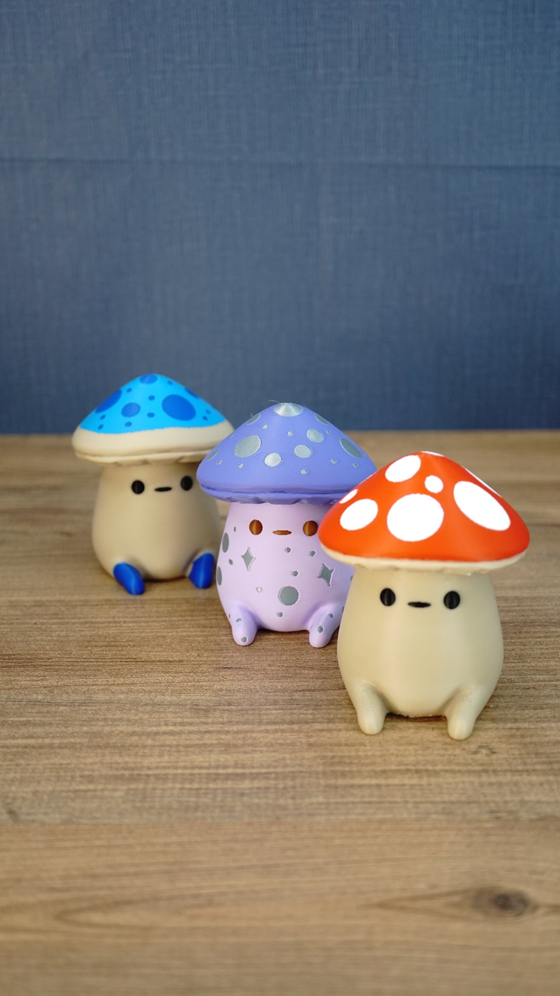 Angled group photo of three Palia Fun Guy figurines with blue, purple, and red mushroom caps on a wooden tabletop.