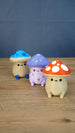 Angled group photo of three Palia Fun Guy figurines with blue, purple, and red mushroom caps on a wooden tabletop.