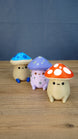 Angled group photo of three Palia Fun Guy figurines with blue, purple, and red mushroom caps on a wooden tabletop.