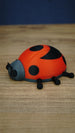 Side angle of the Palia Garden Ladybug Plush collectible showing its rounded red body, black wing markings, grey face and detailed little legs.