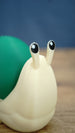Close-up of the Palia Garden Snail Plush figure showing its adorable raised eye stalks, black and white eyes, cream body and green shell