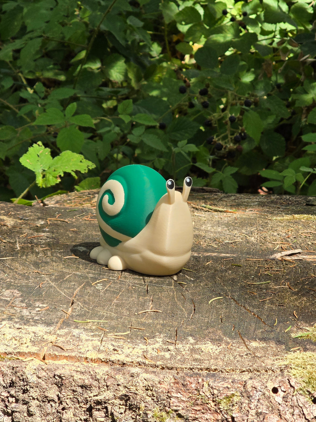 3D printed Palia Garden Snail plush figure with a green spiral shell sitting on a mossy tree stump in the forest.