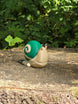 3D printed Palia Garden Snail plush figure with a green spiral shell sitting on a mossy tree stump in the forest.