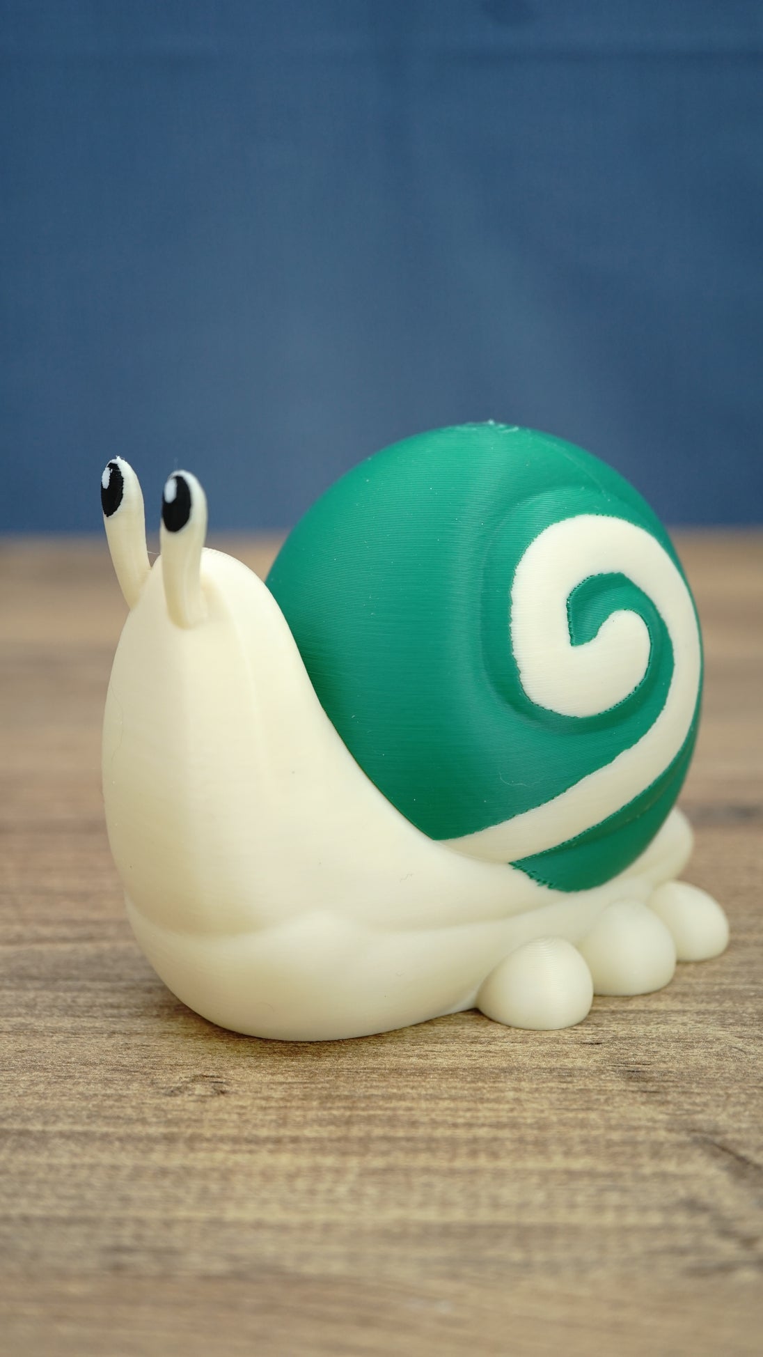 Side view of a Palia Garden Snail Plush figure showing its rounded green shell, cream spiral pattern, cute eye stalks and small snail feet
