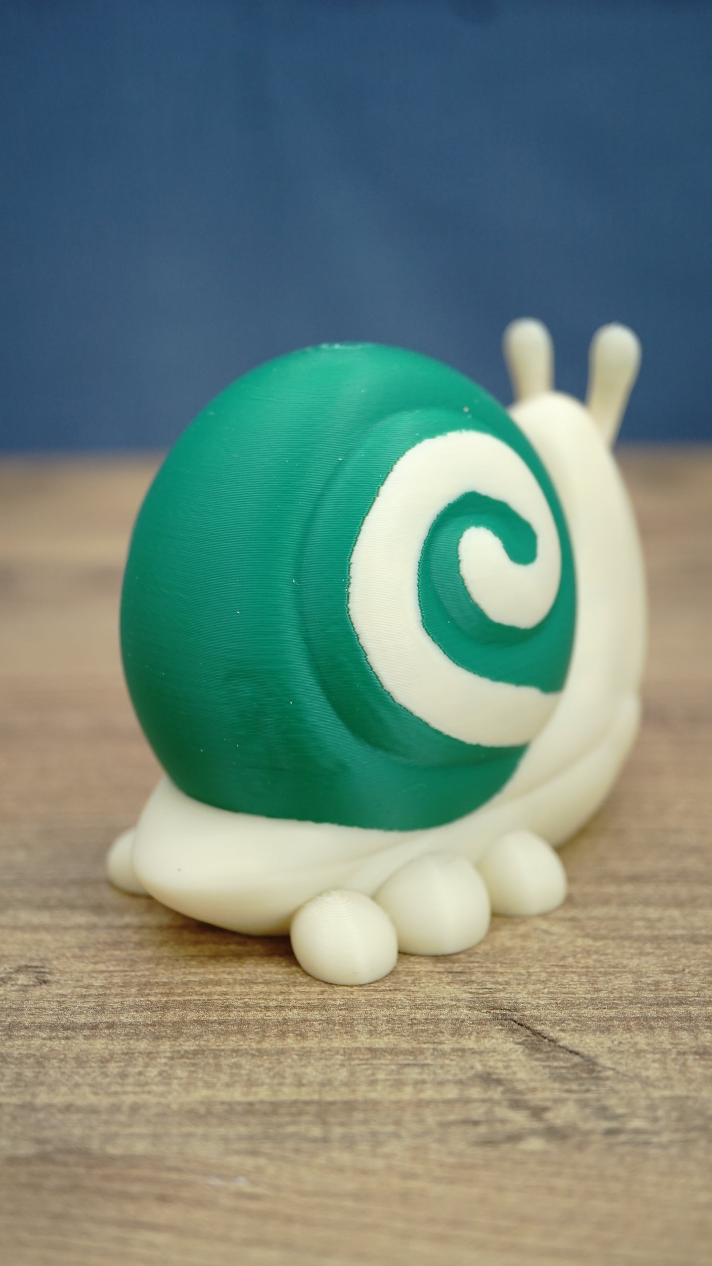 Rear side view of the Palia Garden Snail Plush collectible highlighting the large green shell with cream spiral detail and rounded cream-colored feet