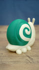 Rear side view of the Palia Garden Snail Plush collectible highlighting the large green shell with cream spiral detail and rounded cream-colored feet