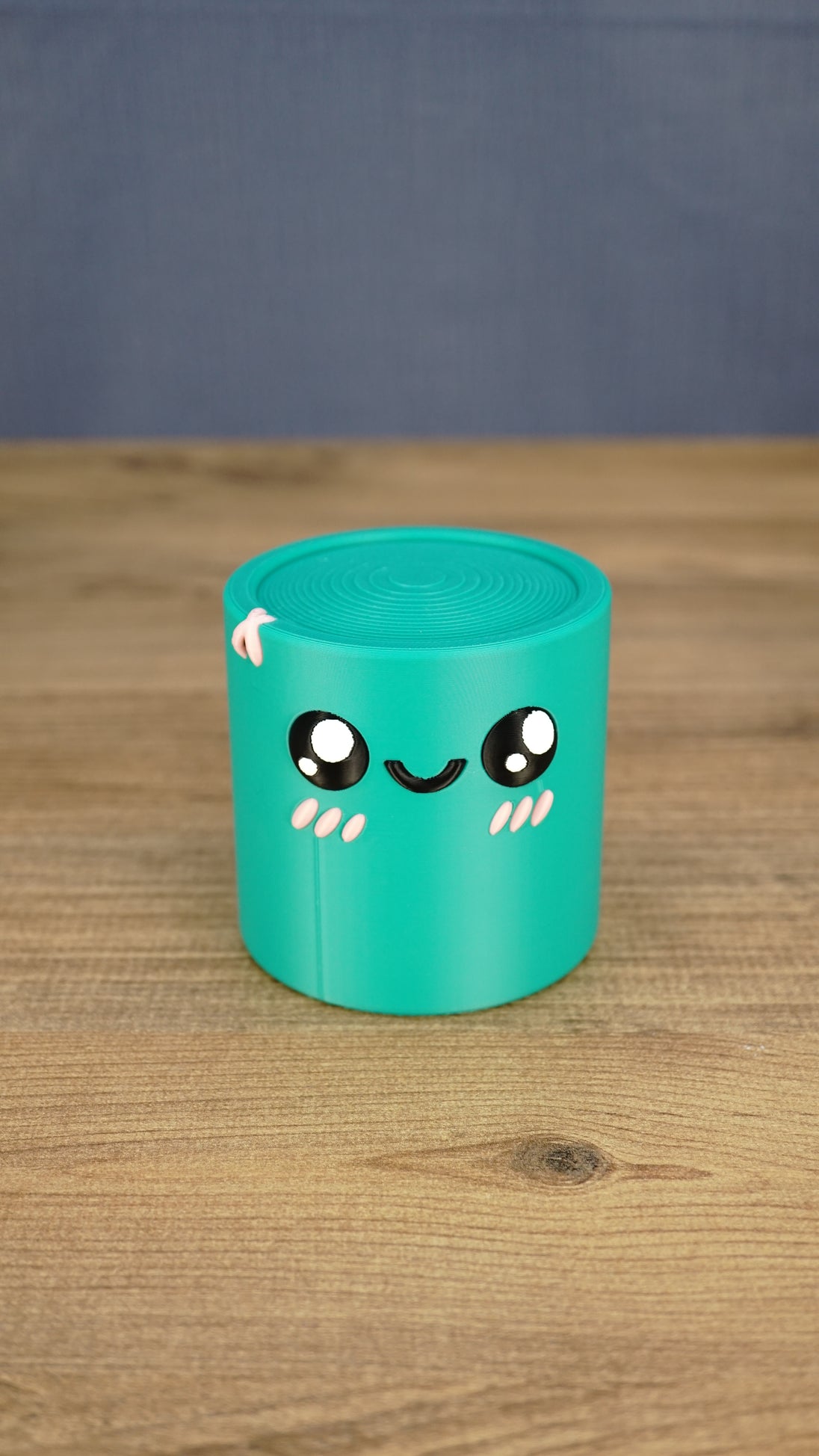 Front view of a teal 3D printed Palia Green Cylinder plush with a cute smiling face, glossy black eyes, and pink cheek details.