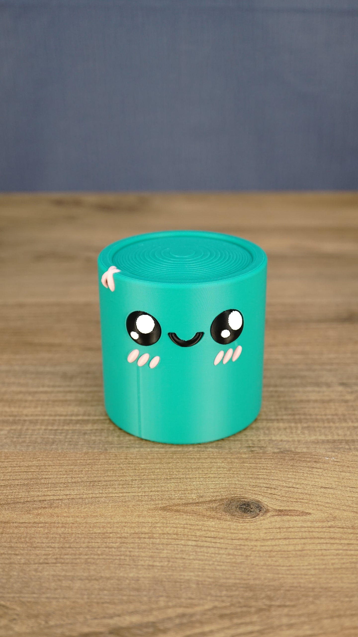 Front view of a teal 3D printed Palia Green Cylinder plush with a cute smiling face, glossy black eyes, and pink cheek details.