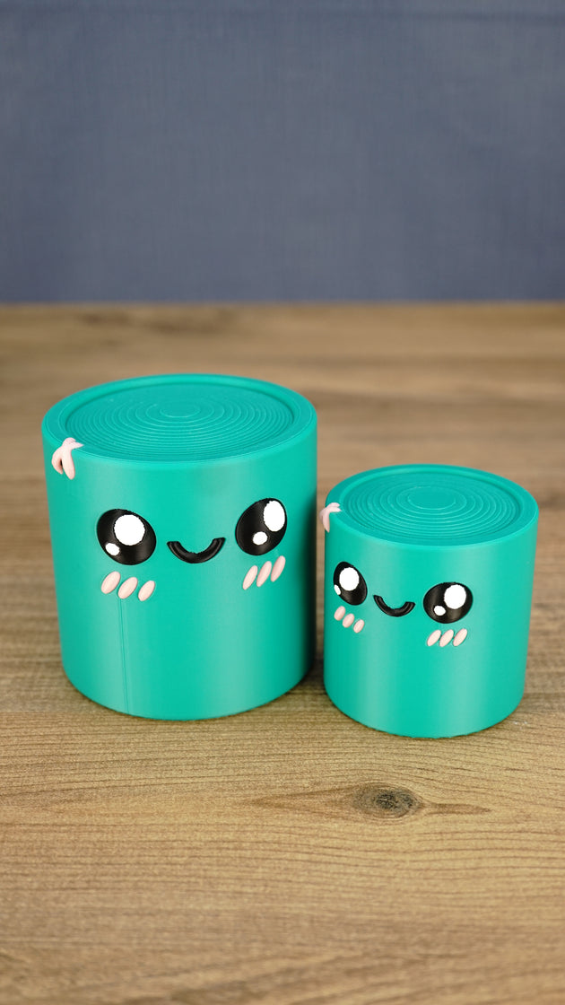 Two teal 3D printed Palia Green Cylinder plush figures in large and small sizes displayed together on a wooden tabletop.