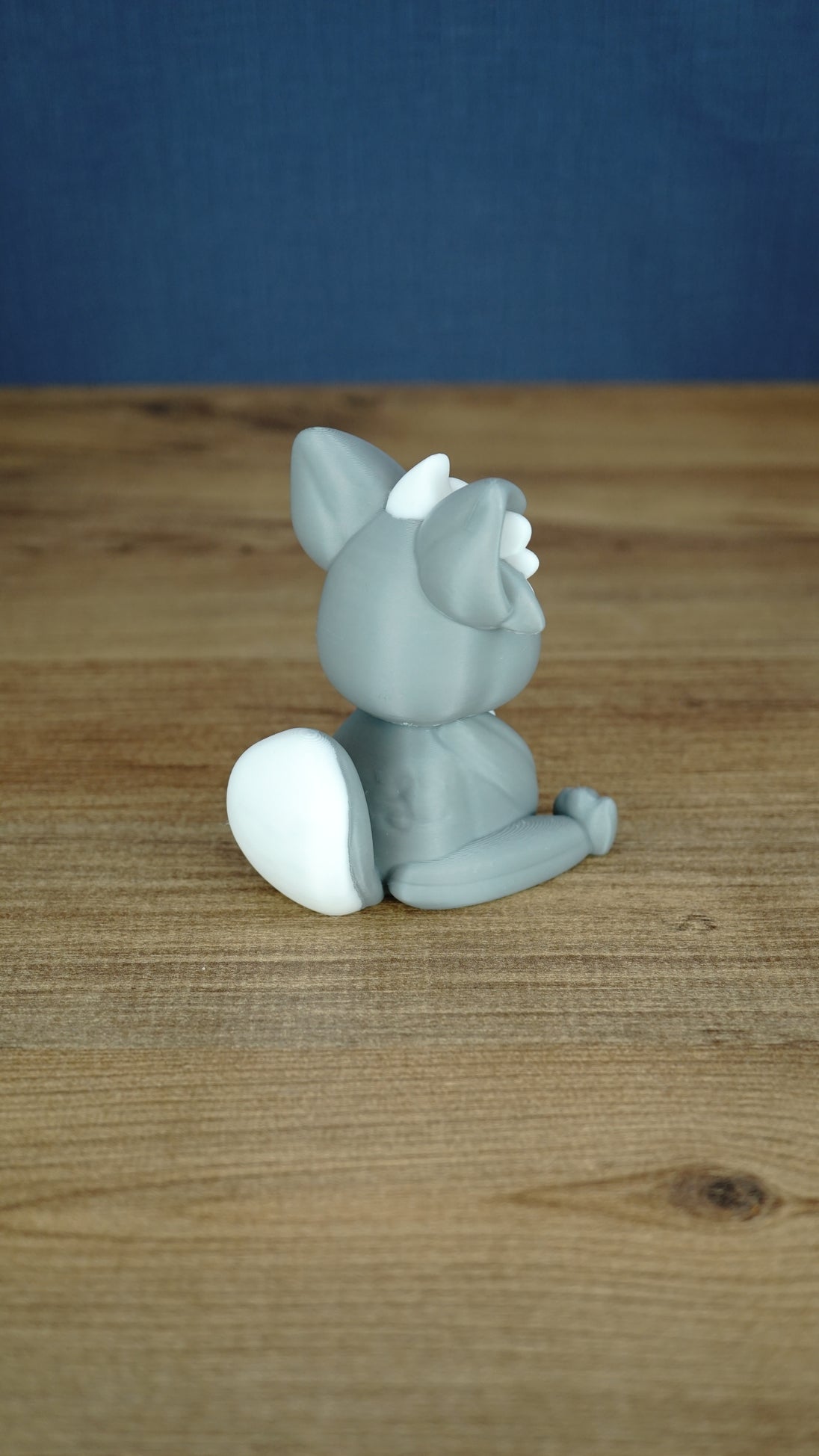Back side view of a grey 3D printed Palcat plush figure showing its curled white-tipped tail, large ears, and seated pose.