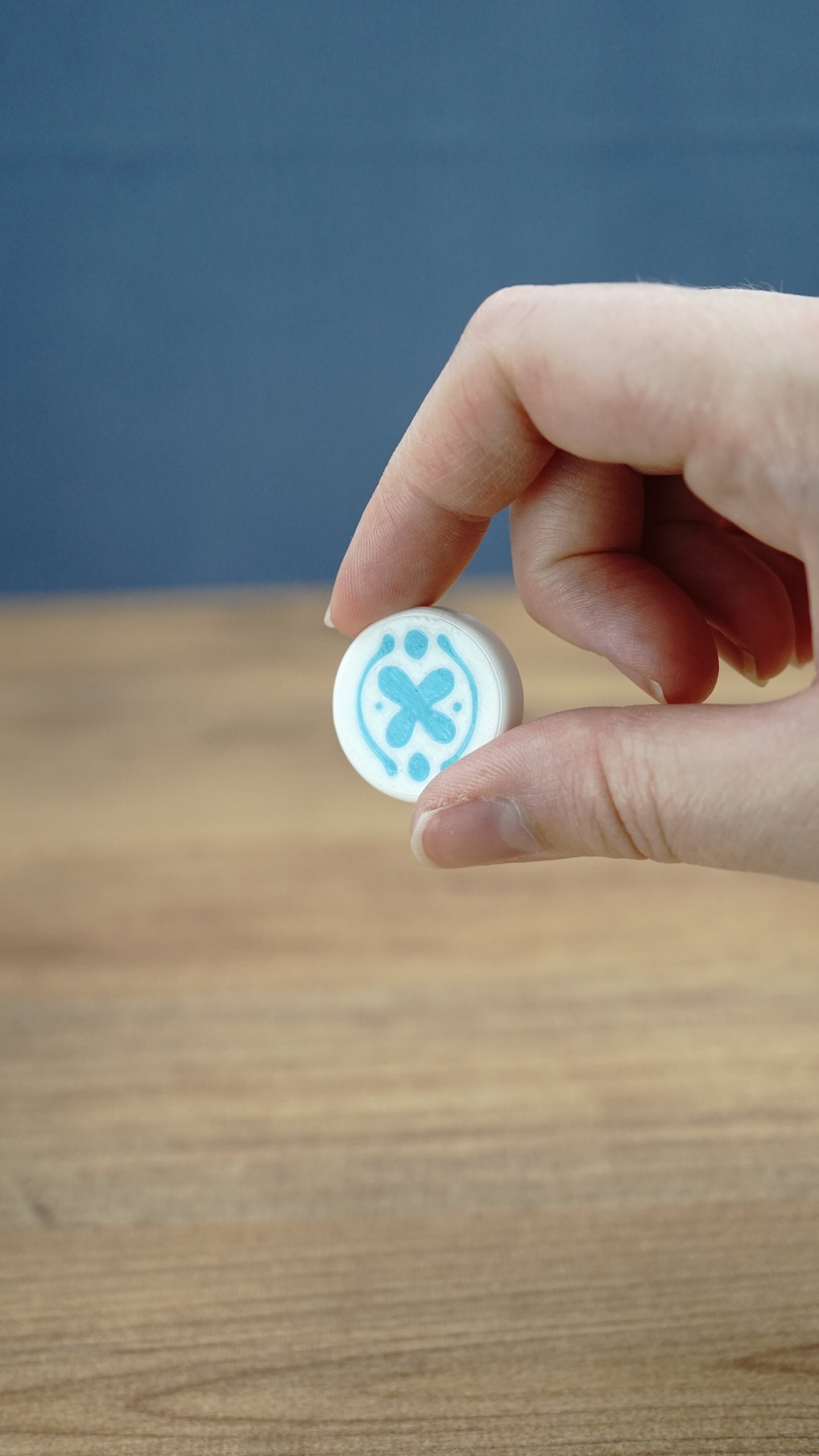 Close-up of a hand holding the white and blue Palia Hotpot pass token against a wooden tabletop background.