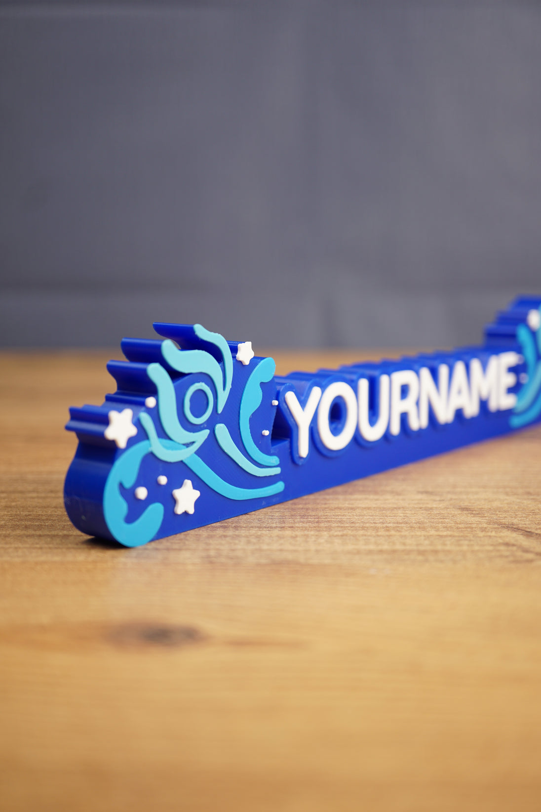 Close side view of a blue custom Palia-style nameplate showing raised white lettering, layered swirl accents, and star details for gamer decor