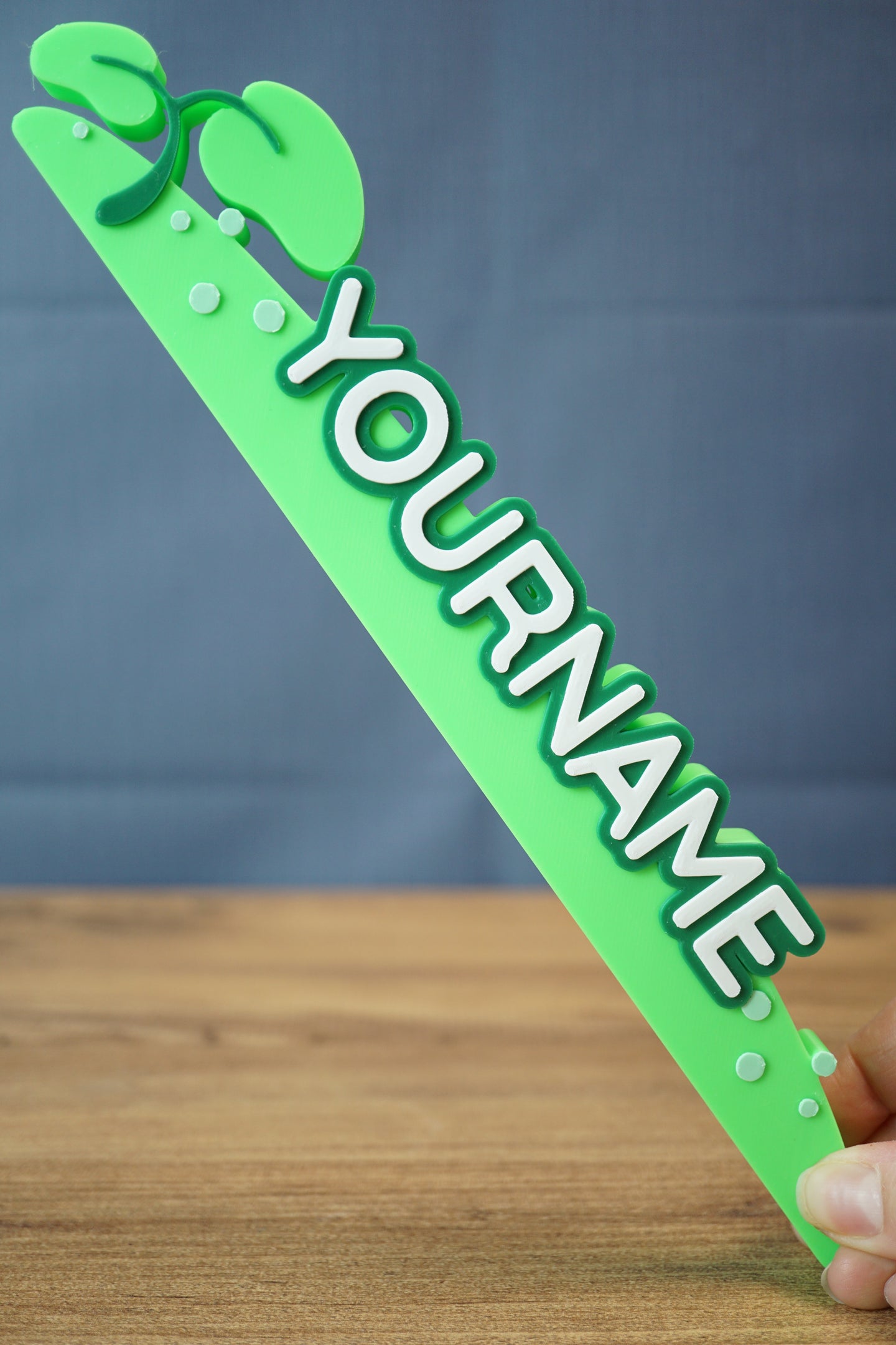 Palia-inspired New in Town nameplate sign held at an angle, showing the full 25cm length, leafy top detail, and raised white lettering.