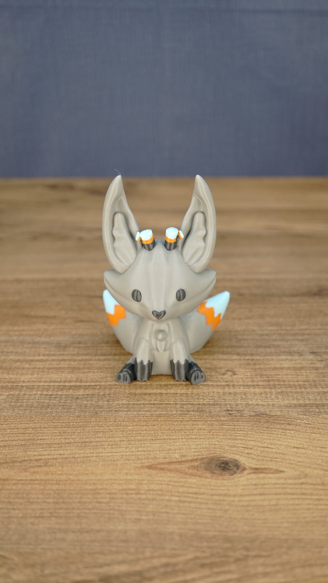 Front view of a gray 3D printed Palia Kitsuu Caldera plush figure with tall ears, dark paws, and orange and white tail details.