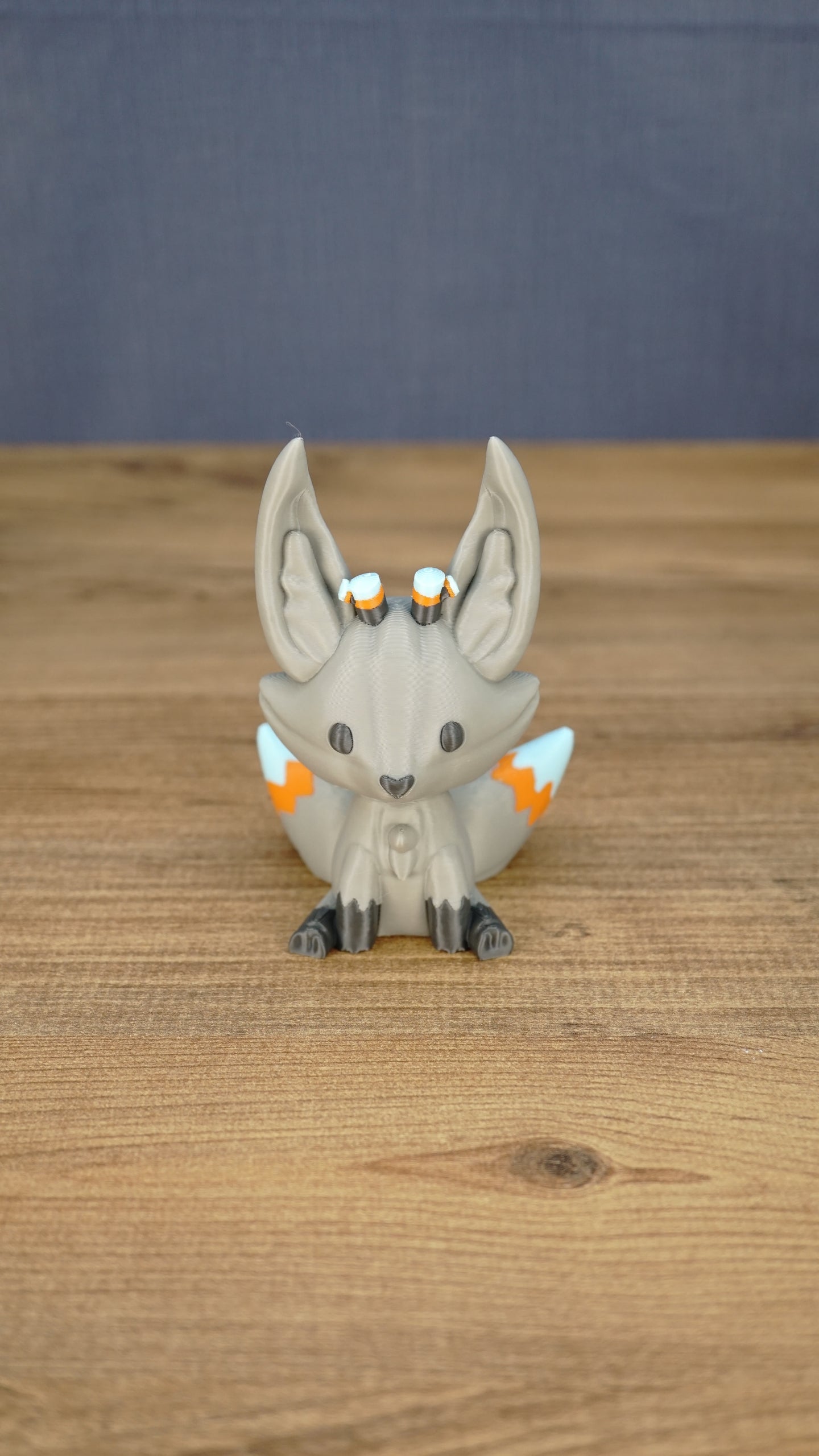 Front view of a gray 3D printed Palia Kitsuu Caldera plush figure with tall ears, dark paws, and orange and white tail details.