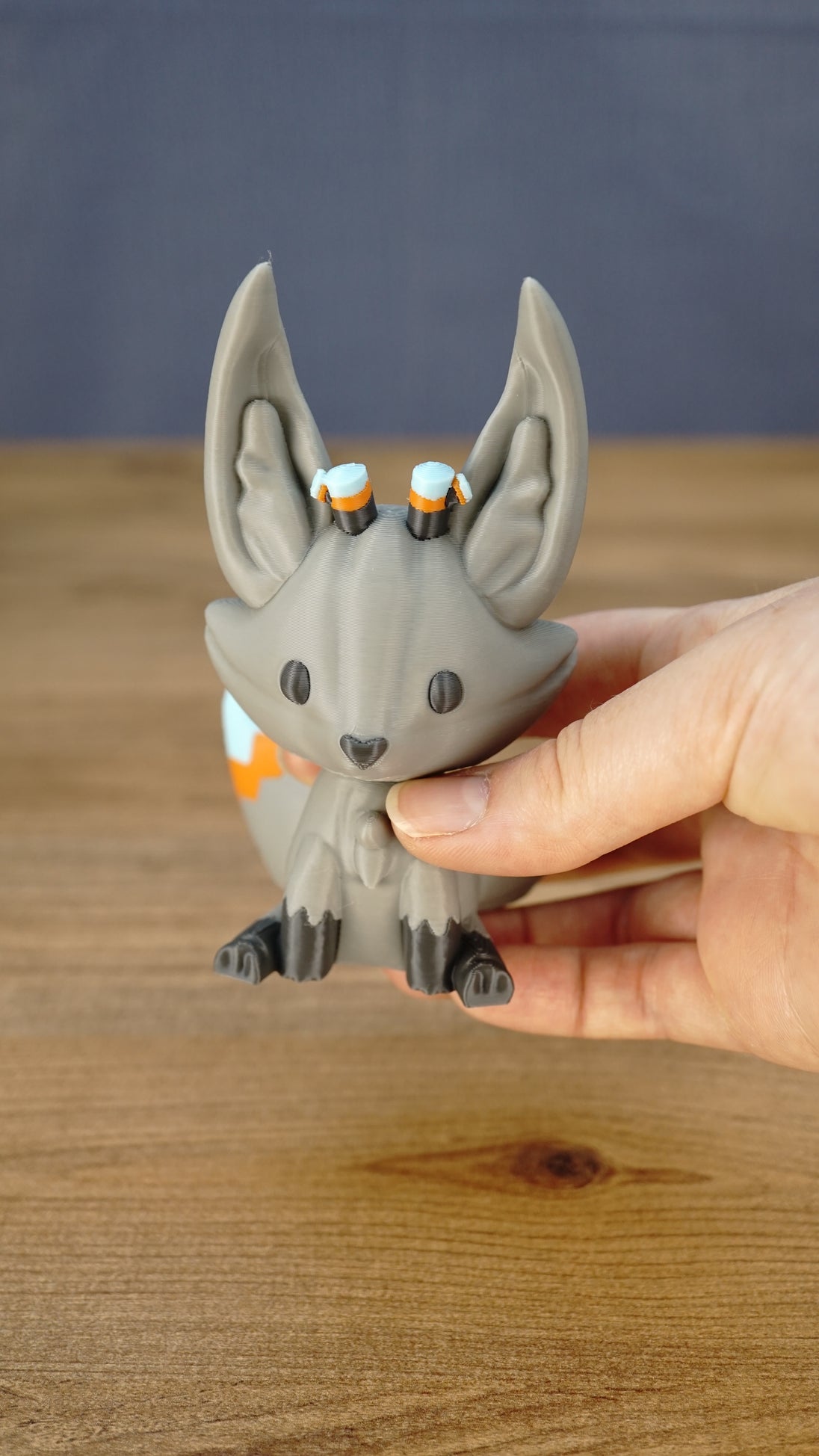 Close-up of a Palia Kitsuu Caldera plush figure being held, showing its gray face, tall ears, small horns, and dark paw details.