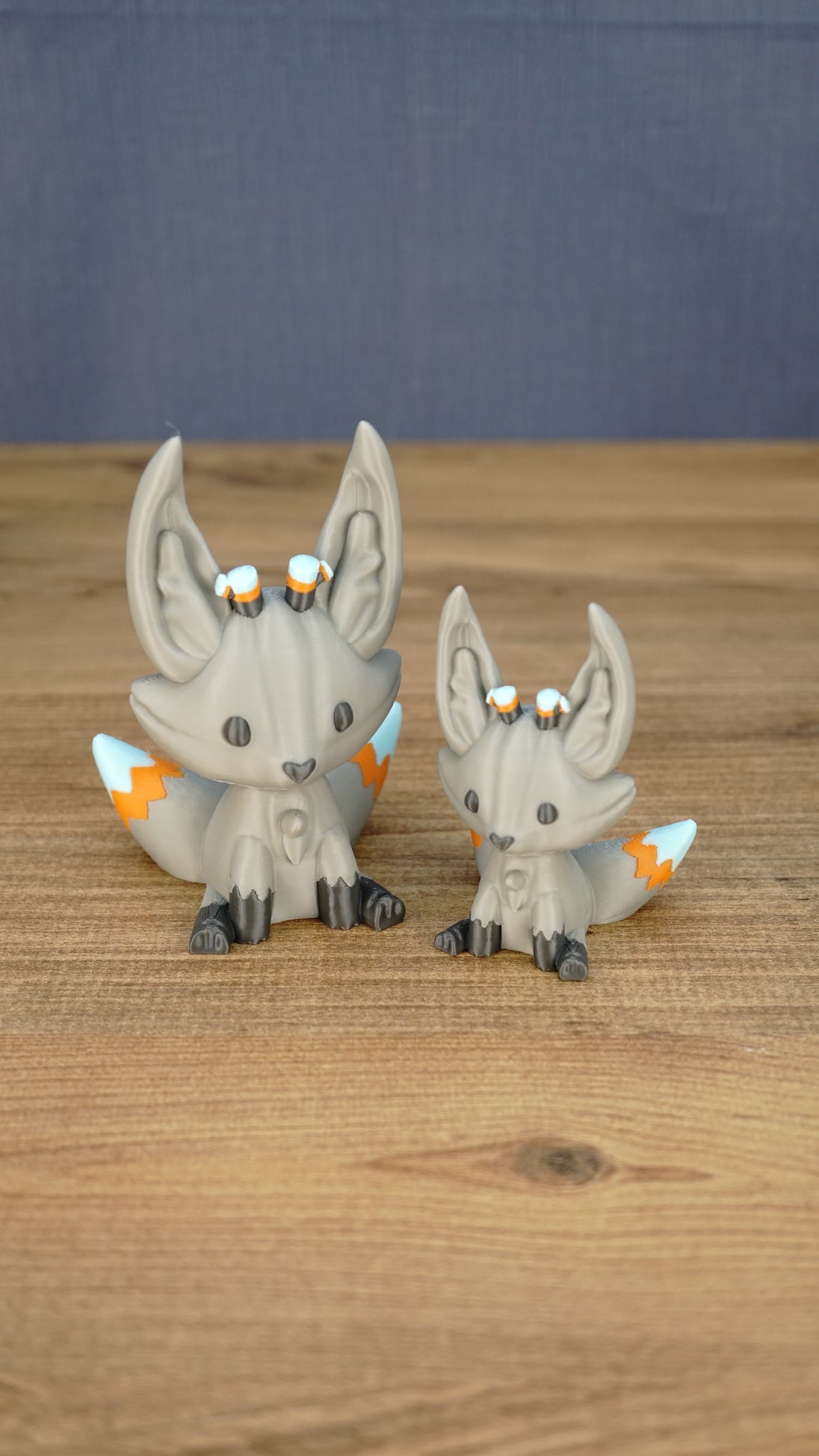Two gray Palia Kitsuu Caldera plush figures in small and large sizes displayed together on a wooden tabletop.