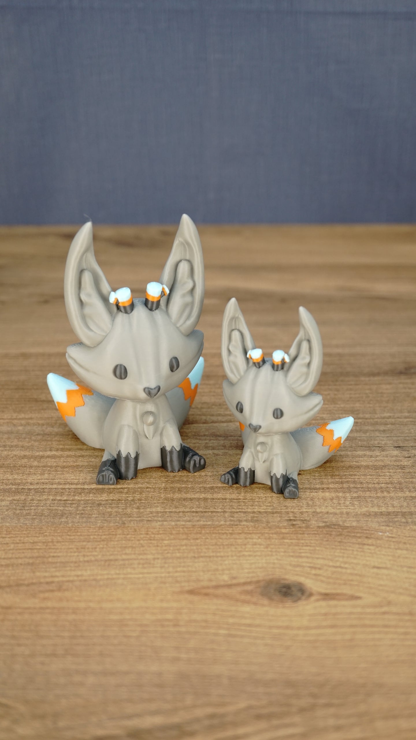 Two gray Palia Kitsuu Caldera plush figures in small and large sizes displayed together on a wooden tabletop.