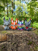 Four 3D printed Palia Kitsuu figures in ancient, orange, rainbow, and obsidian colourways displayed on a tree stump in a forest.