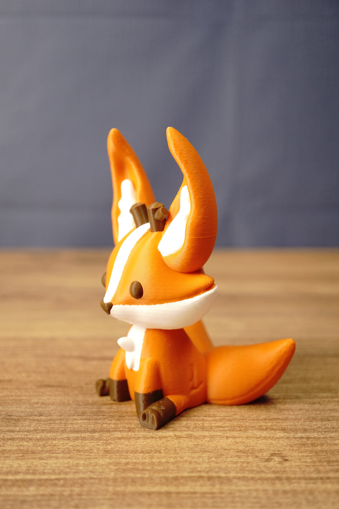 Side view of an Ancient Kitsuu-inspired 3D-printed fox figure showing its tall ears, white facial markings, and large orange tail.
