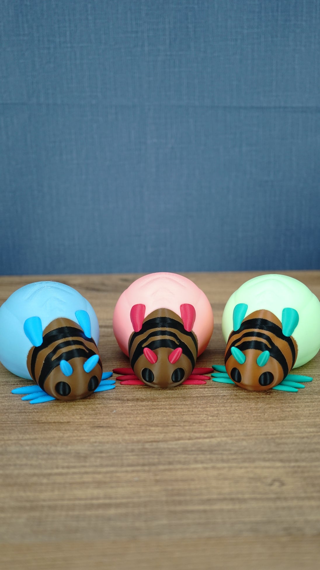 Pink, blue, and green Palia-inspired lantern bug plush figures lined up together on a wooden tabletop.