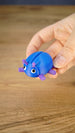 Hand holding the blue and purple Li’l Beetle miniature, showing its rounded shell, six legs, antennae and expressive white eyes.