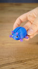 Hand holding the blue and purple Li’l Beetle miniature, showing its rounded shell, six legs, antennae and expressive white eyes.